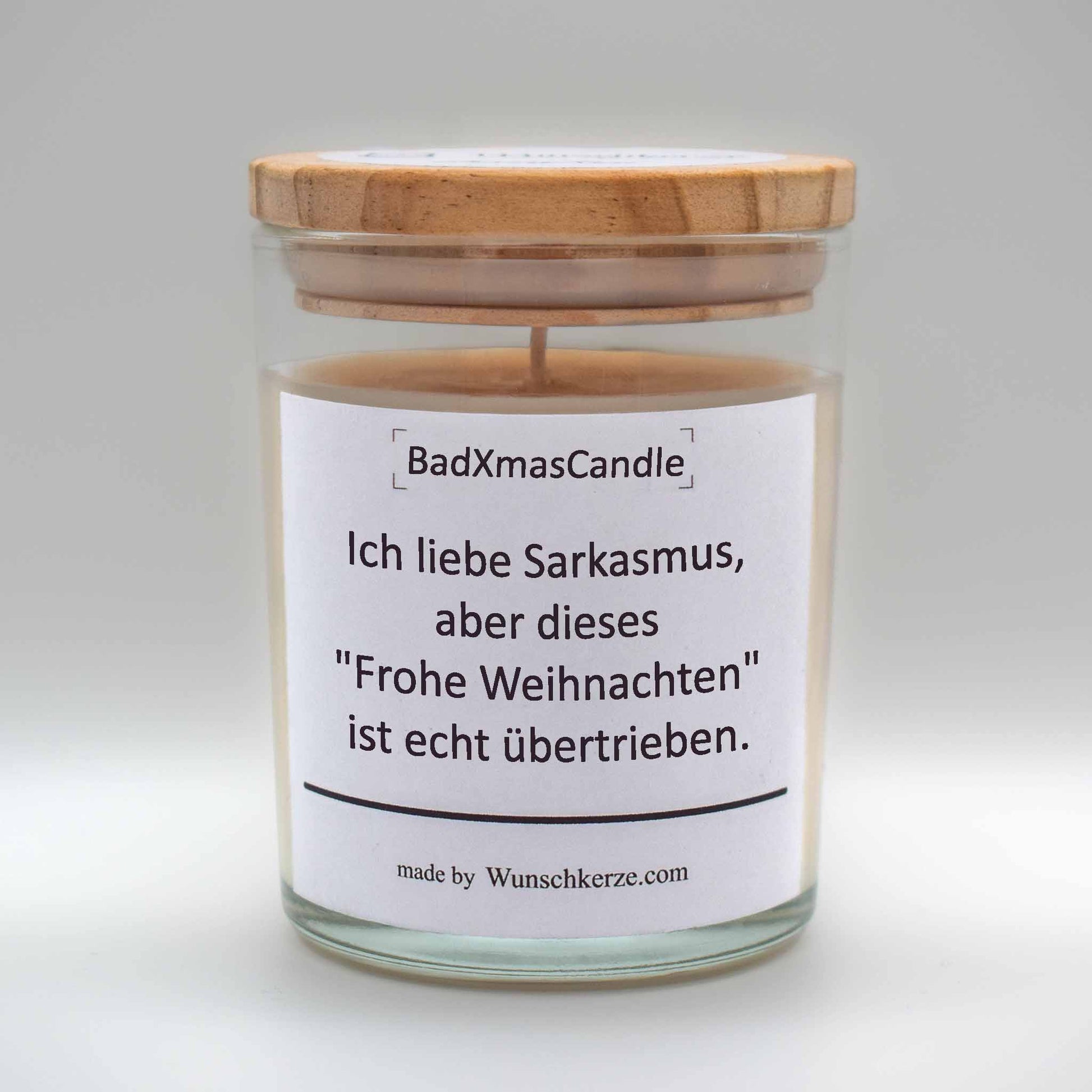 Soja Duftkerze im Glas mit Deckel aus Kiefernholz mit einem Label. Aufschrift: BadXmasCandle - Ich liebe Sarkasmus, aber dieses "Frohe Weihnachten" ist echt übertrieben.